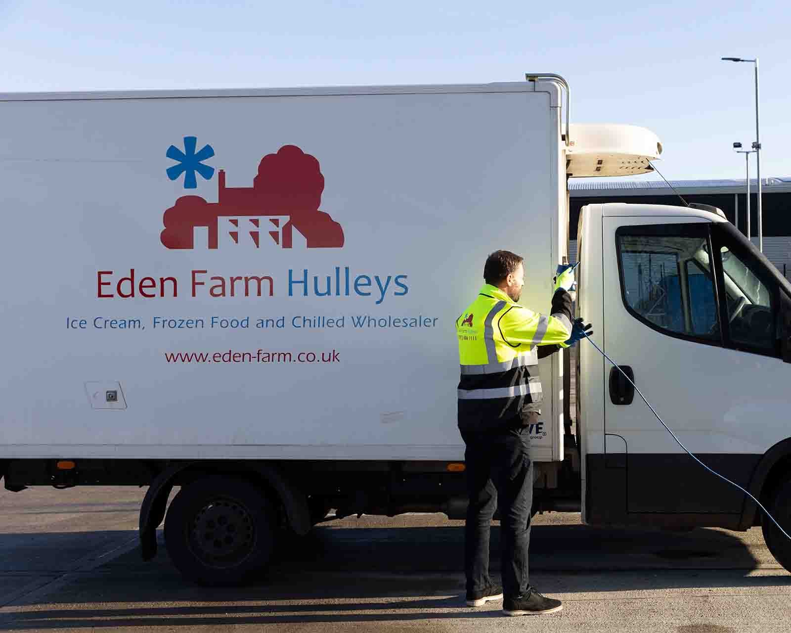 Worker in a high-visibility jacket cleaning a refrigerated delivery truck branded with Eden Farm Hulleys